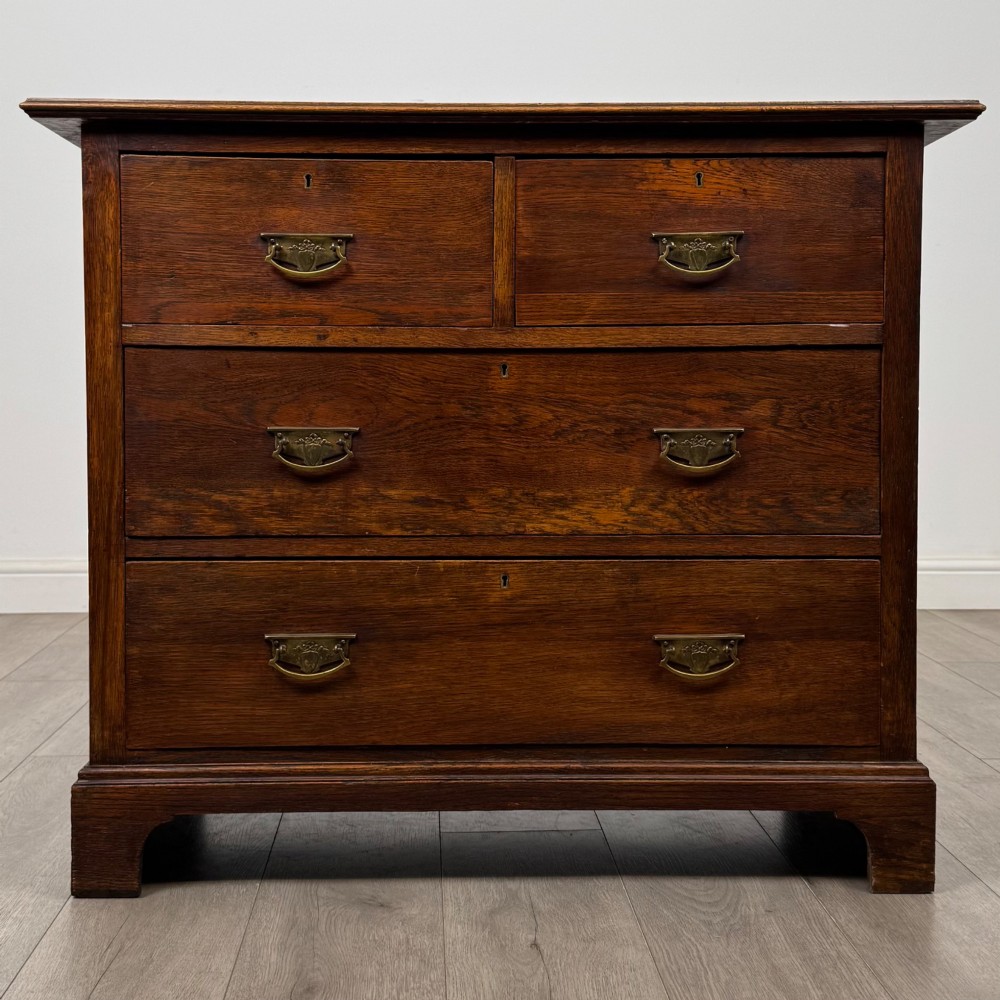 An antique Edwardian dark oak chest of drawers featuring two small top drawers above two full-width drawers with brass handles.