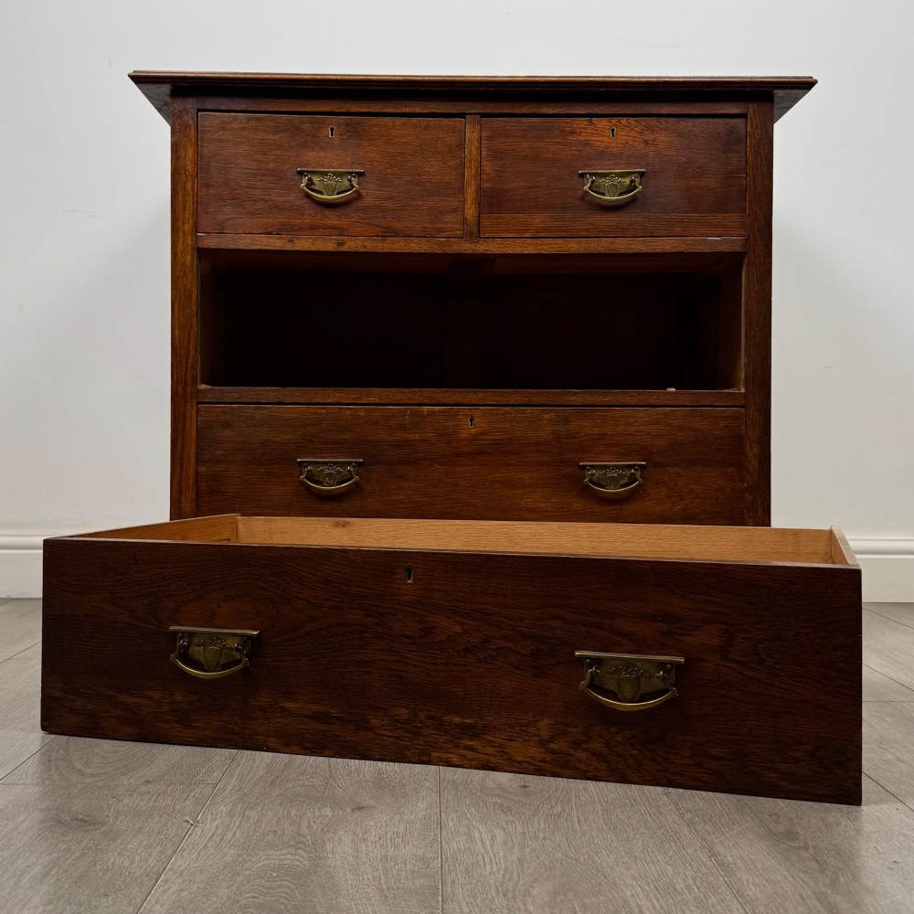 An antique Edwardian dark oak chest of drawers featuring two small top drawers above two full-width drawers with brass handles. View X