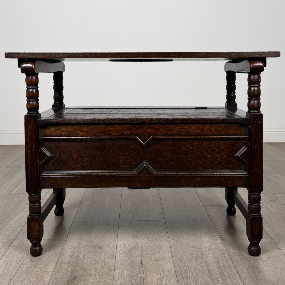 A dark oak monks bench featuring a panelled backrest with a central diamond motif, turned arm supports, and a lift-up seat. View II