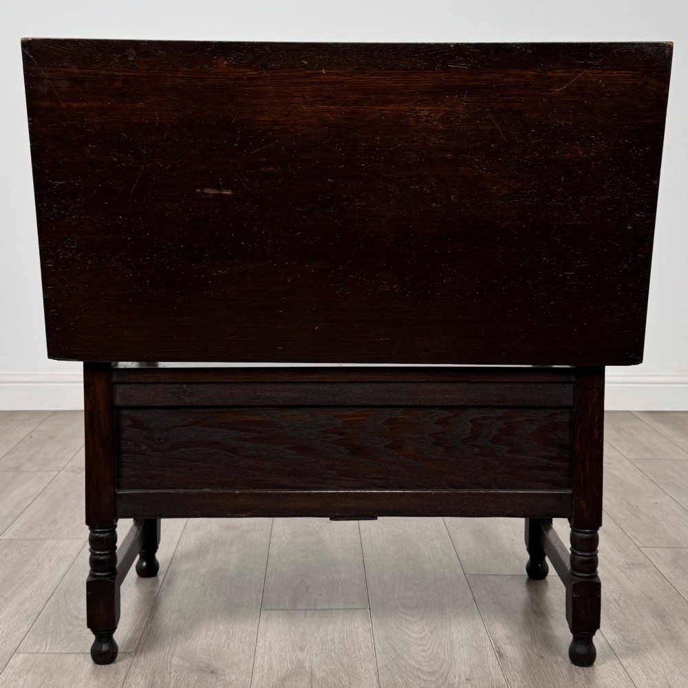 A dark oak monks bench featuring a panelled backrest with a central diamond motif, turned arm supports, and a lift-up seat. View VI