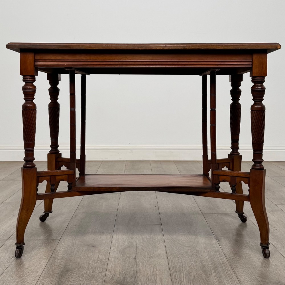An Edwardian walnut side table featuring turned spiral legs, a lower shelf, carved corner brackets, and metal castors.