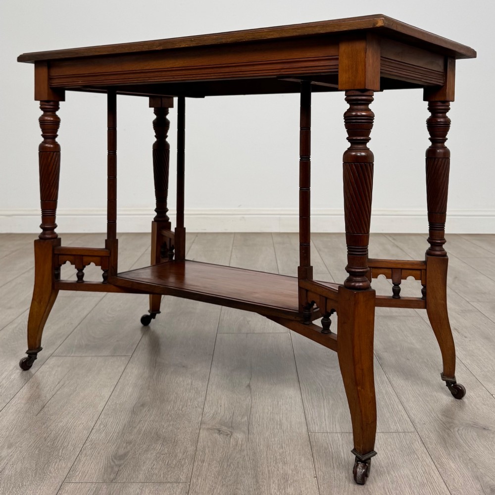 An Edwardian walnut side table featuring turned spiral legs, a lower shelf, carved corner brackets, and metal castors. View II