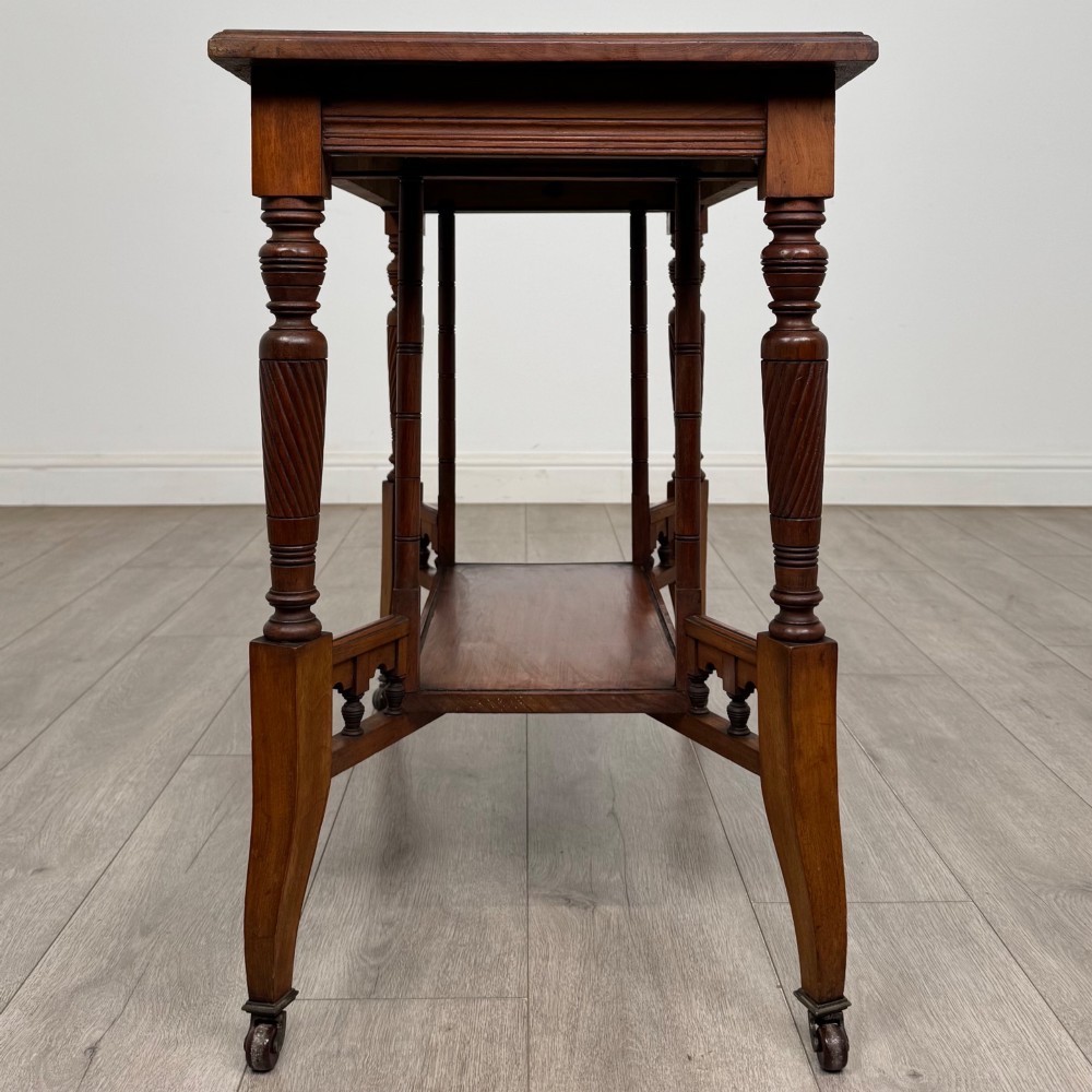 An Edwardian walnut side table featuring turned spiral legs, a lower shelf, carved corner brackets, and metal castors. View III