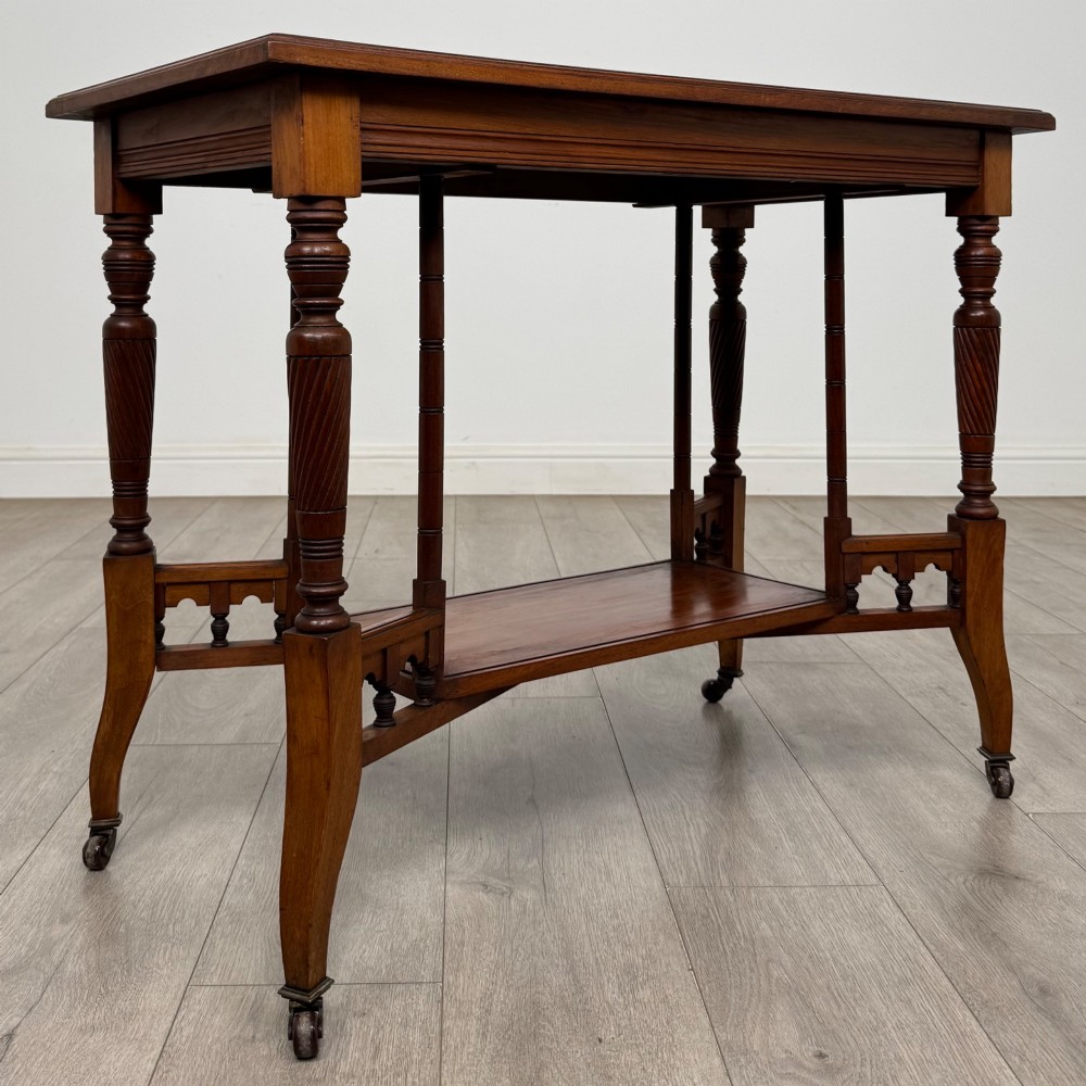 An Edwardian walnut side table featuring turned spiral legs, a lower shelf, carved corner brackets, and metal castors. View IV