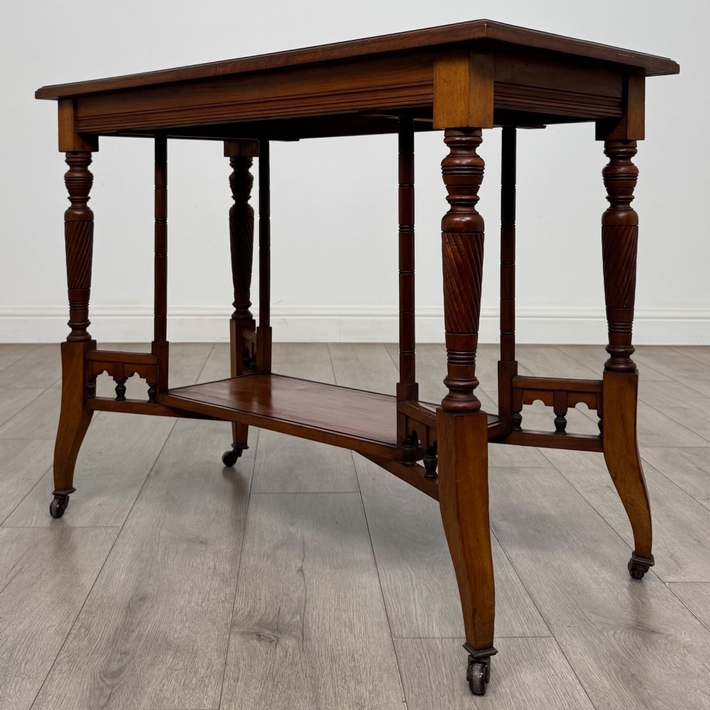 An Edwardian walnut side table featuring turned spiral legs, a lower shelf, carved corner brackets, and metal castors. View VI