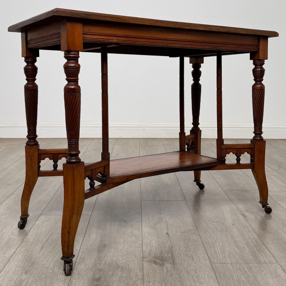 An Edwardian walnut side table featuring turned spiral legs, a lower shelf, carved corner brackets, and metal castors. View VIII