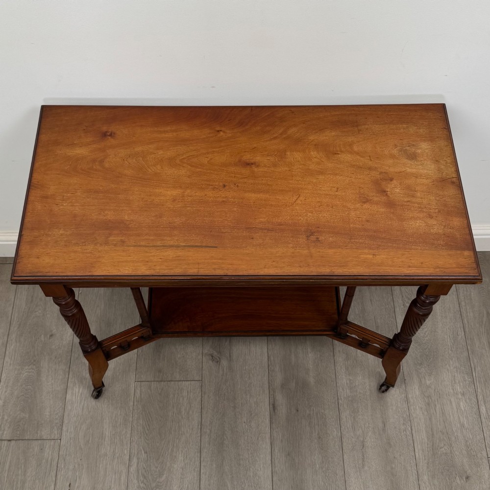 An Edwardian walnut side table featuring turned spiral legs, a lower shelf, carved corner brackets, and metal castors. View IX