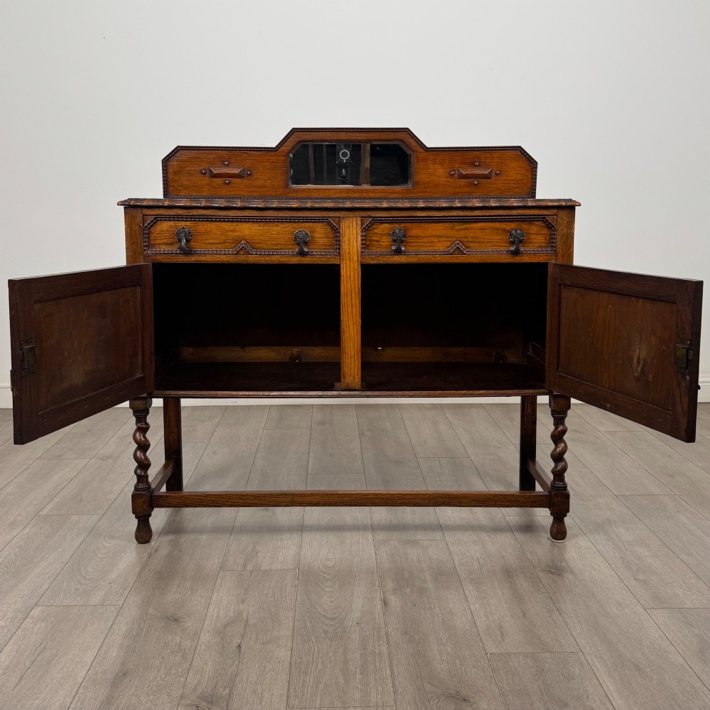 An Edwardian golden oak sideboard featuring a raised mirror back gallery, two drawers, two cabinet doors with geometric mouldings, and barley twist front legs. View II