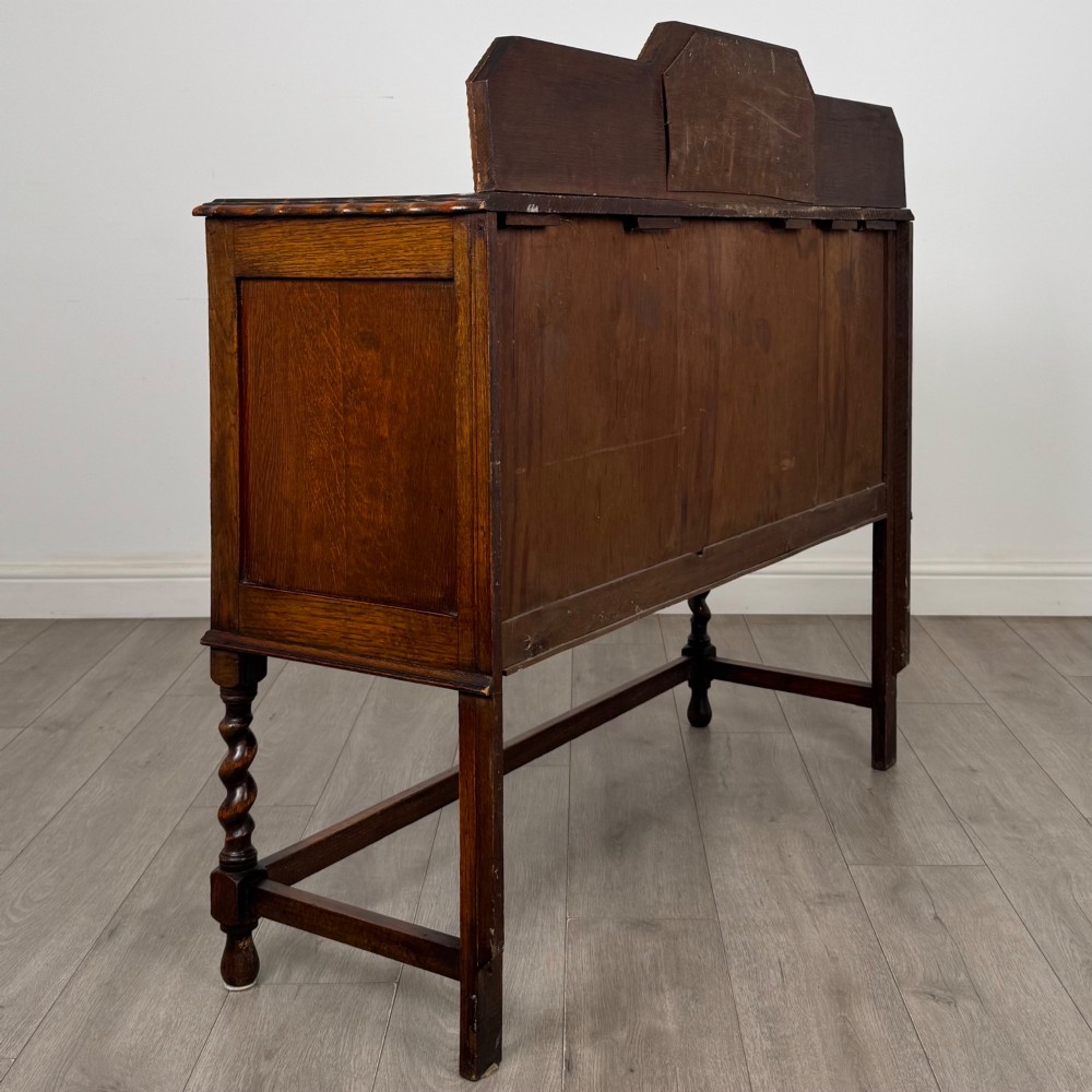 An Edwardian golden oak sideboard featuring a raised mirror back gallery, two drawers, two cabinet doors with geometric mouldings, and barley twist front legs. View V