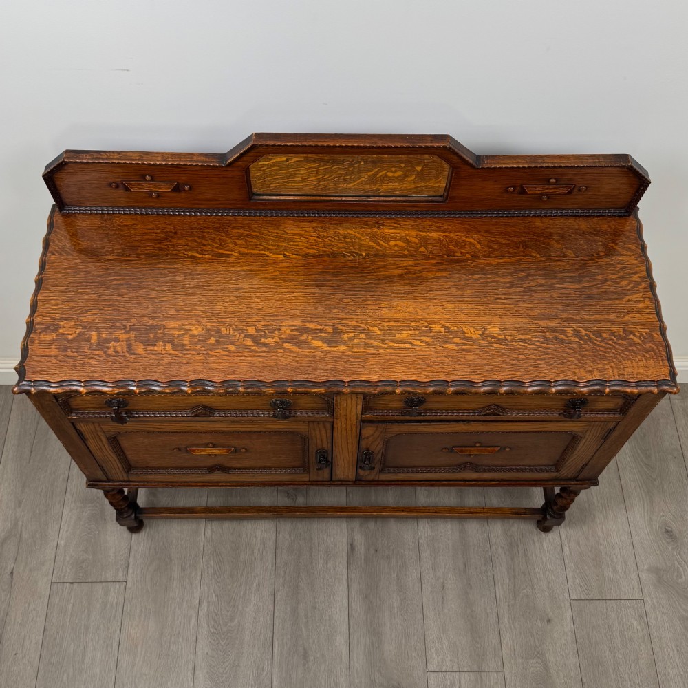 An Edwardian golden oak sideboard featuring a raised mirror back gallery, two drawers, two cabinet doors with geometric mouldings, and barley twist front legs. View X
