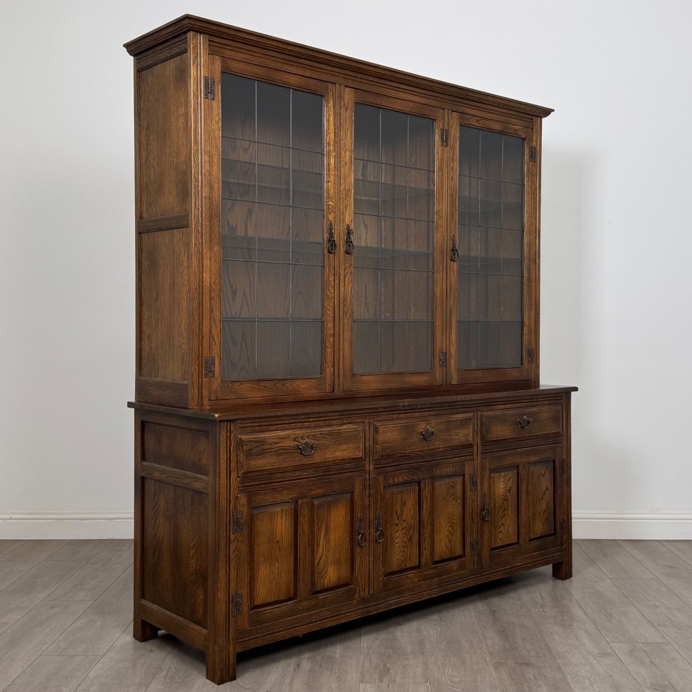 A large dark oak display cabinet featuring three leaded glass doors above three drawers and three panelled cupboard doors. View IX