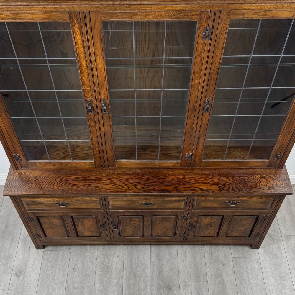 A large dark oak display cabinet featuring three leaded glass doors above three drawers and three panelled cupboard doors. View X