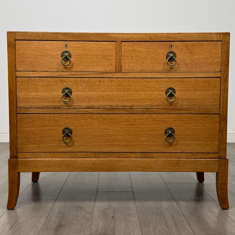 A golden oak chest of drawers featuring two short drawers over two long drawers with brass ring handles.