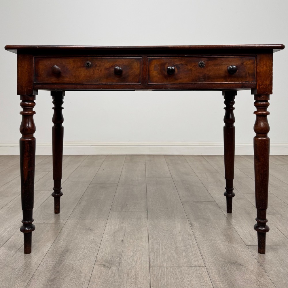 A Victorian dark mahogany writing table with two drawers, turned wooden knob handles, keyhole escutcheons, and four turned legs.