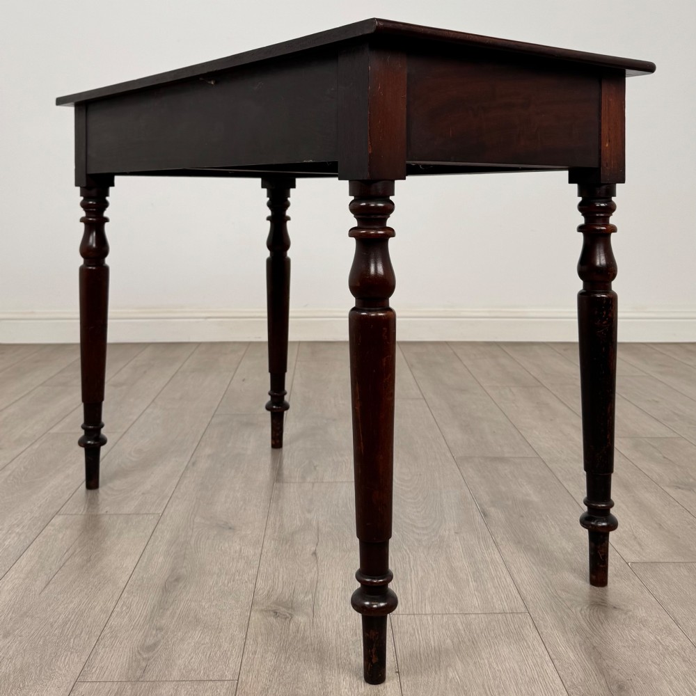 A Victorian dark mahogany writing table with two drawers, turned wooden knob handles, keyhole escutcheons, and four turned legs. View VI