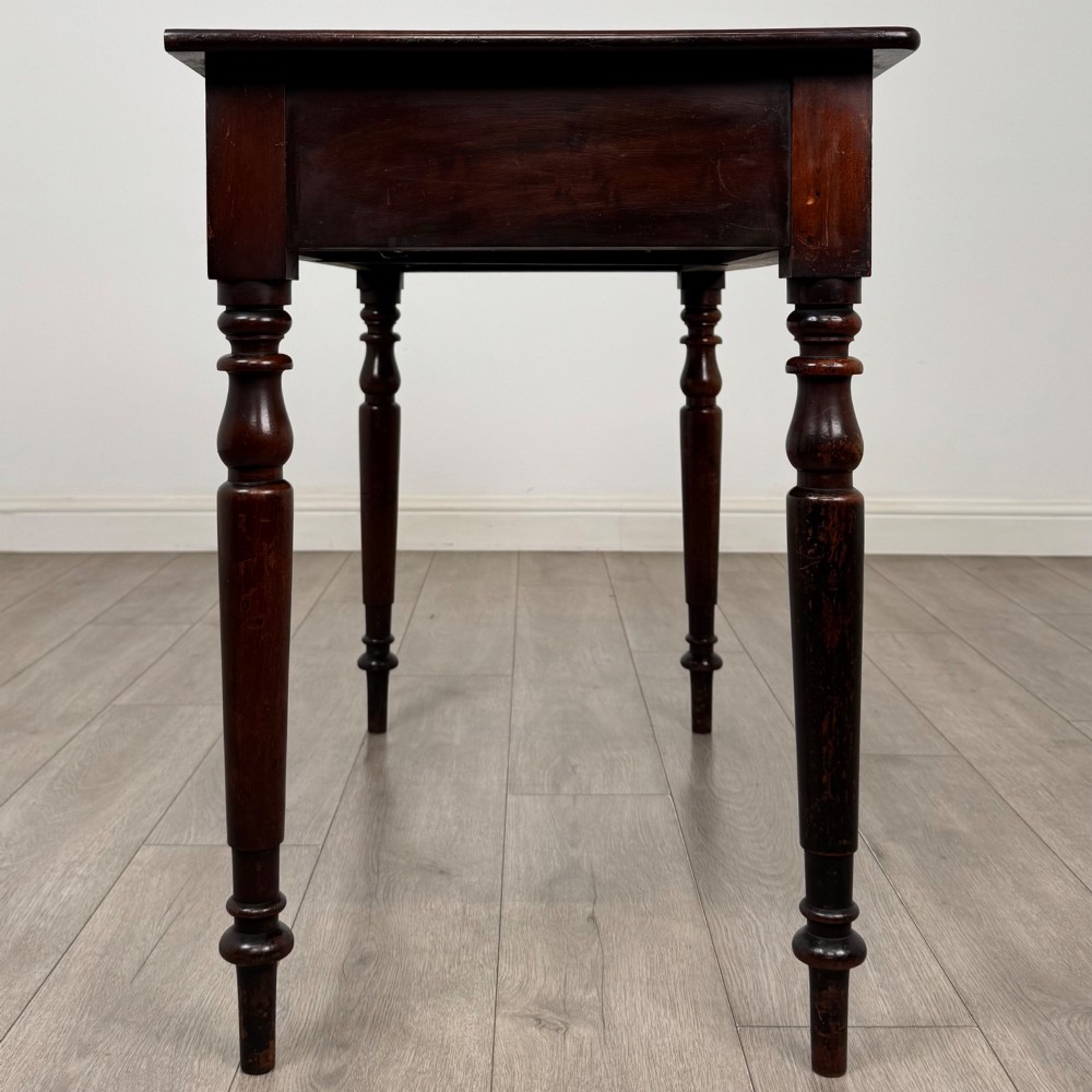 A Victorian dark mahogany writing table with two drawers, turned wooden knob handles, keyhole escutcheons, and four turned legs. View VII