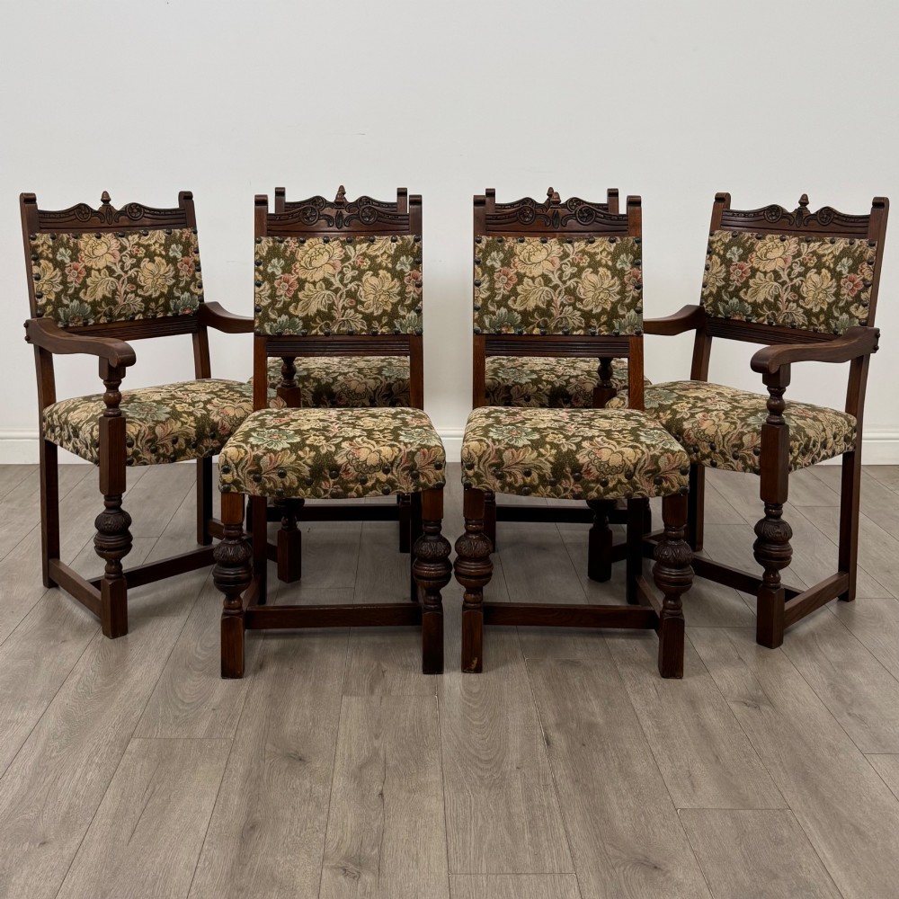 A set of six dark oak dining chairs with carved crest rails, floral tapestry upholstered backrests and seats, and turned front legs.