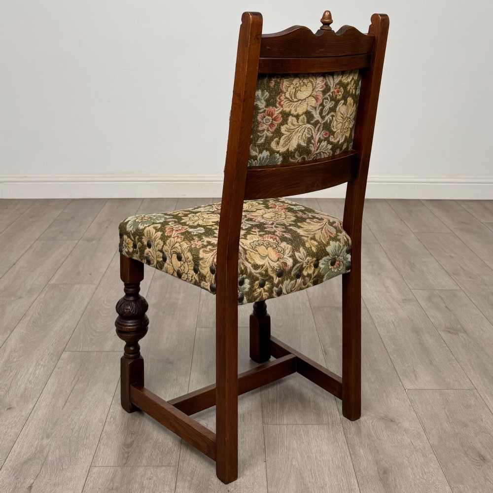 A set of six dark oak dining chairs with carved crest rails, floral tapestry upholstered backrests and seats, and turned front legs. View IV