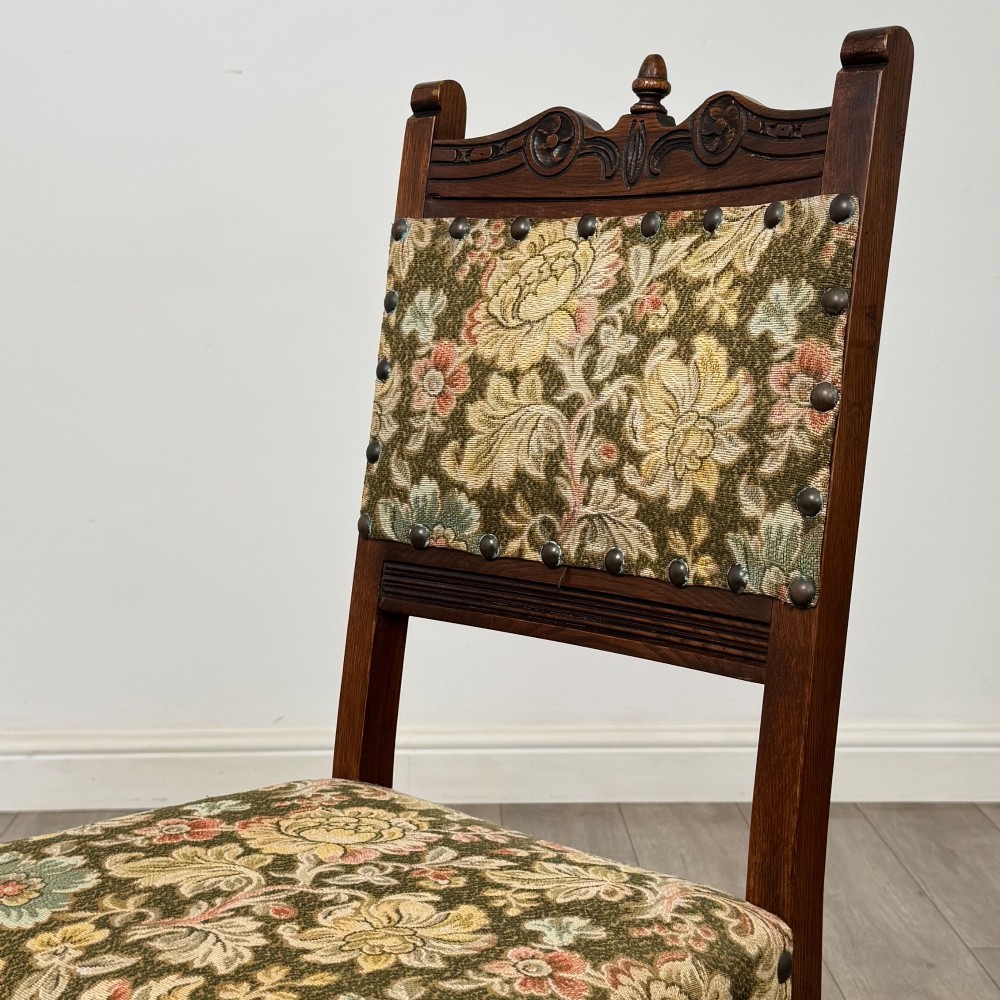 A set of six dark oak dining chairs with carved crest rails, floral tapestry upholstered backrests and seats, and turned front legs. View V