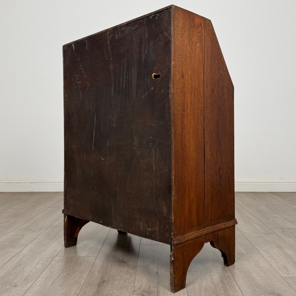An Edwardian oak bureau featuring a slanted fall-front lid above three drawers with decorative circular brass drop handles. View VII