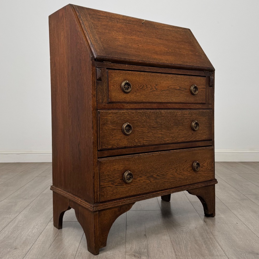 An Edwardian oak bureau featuring a slanted fall-front lid above three drawers with decorative circular brass drop handles. View IX