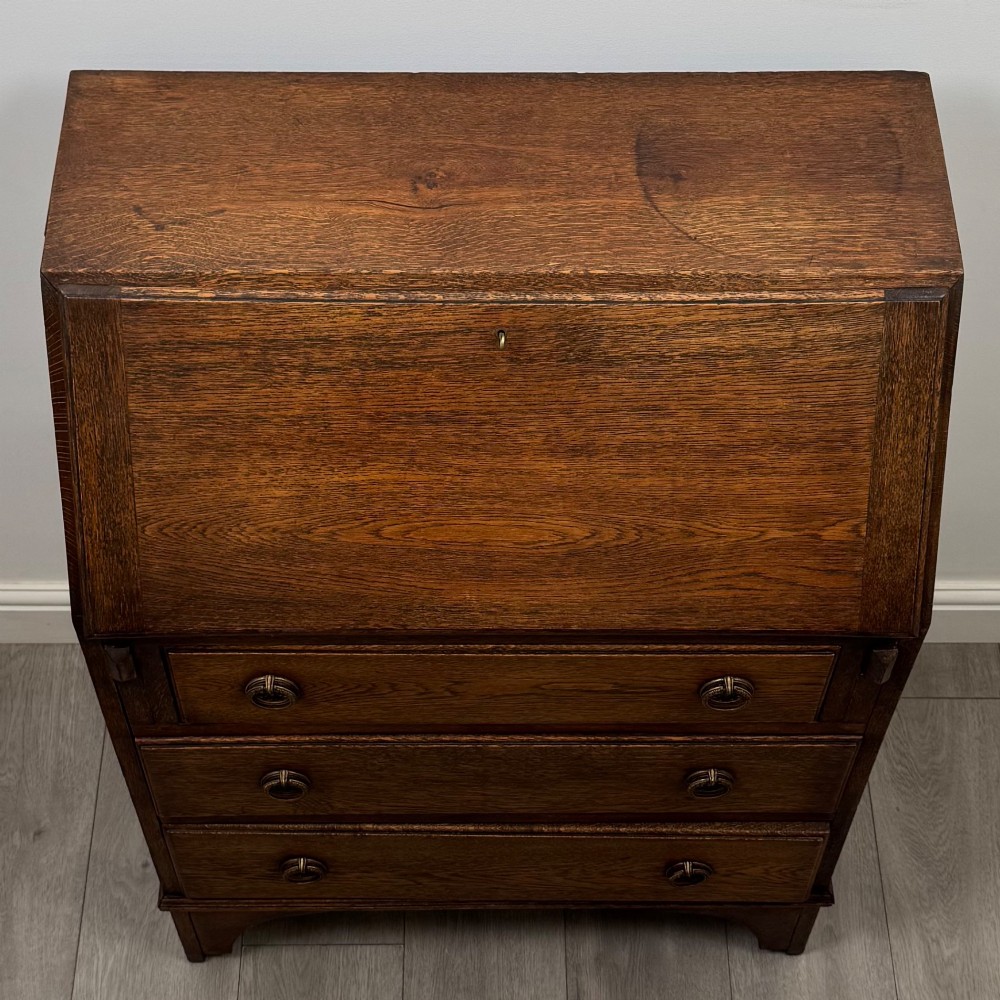 An Edwardian oak bureau featuring a slanted fall-front lid above three drawers with decorative circular brass drop handles. View X
