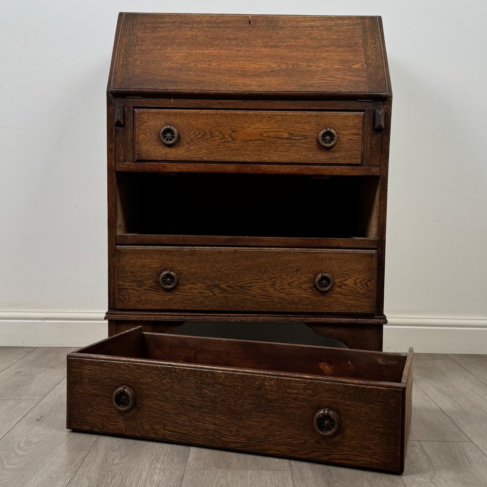 An Edwardian oak bureau featuring a slanted fall-front lid above three drawers with decorative circular brass drop handles. View XII