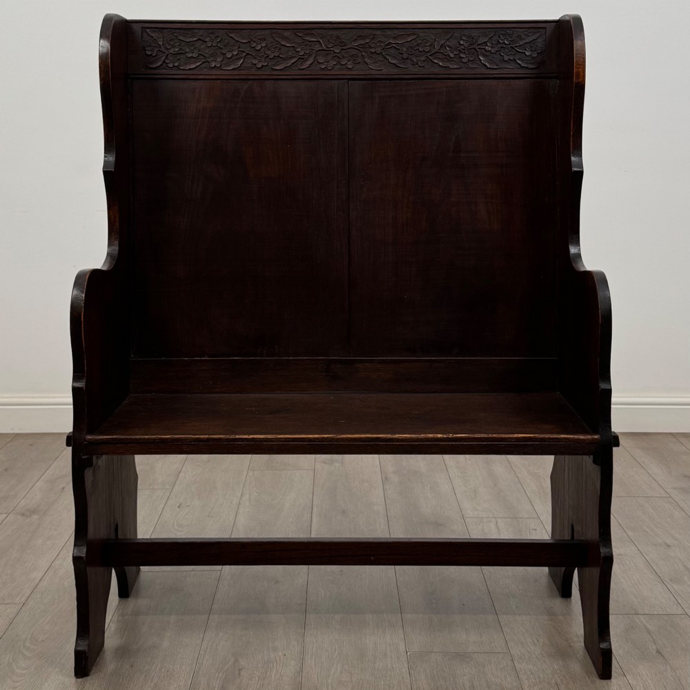 A dark oak high-back settle featuring a floral relief carving along the top rail, shaped side panels, and a stretcher base.