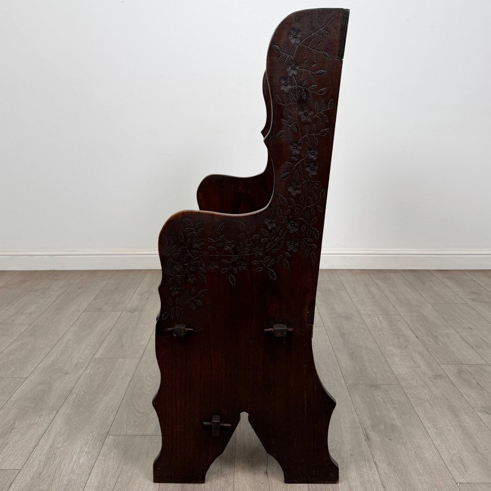 A dark oak high-back settle featuring a floral relief carving along the top rail, shaped side panels, and a stretcher base. View III