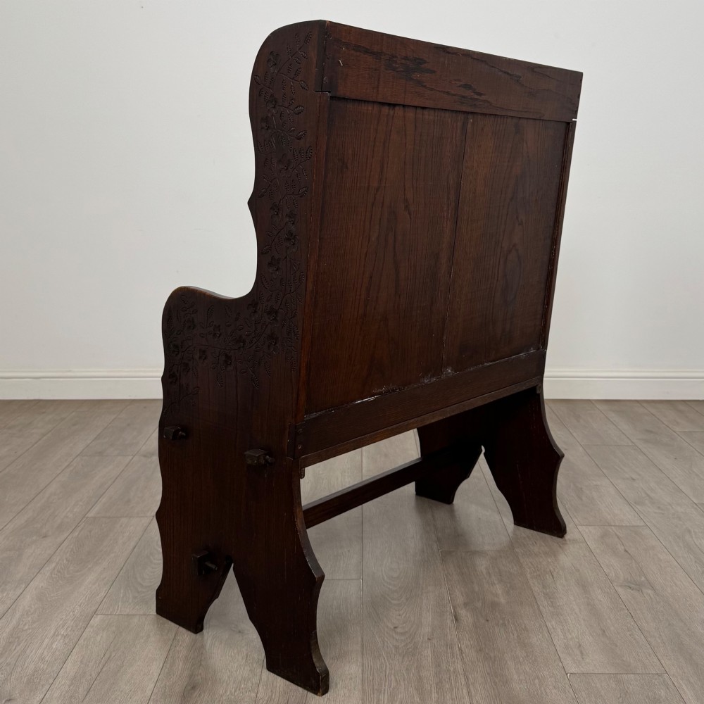 A dark oak high-back settle featuring a floral relief carving along the top rail, shaped side panels, and a stretcher base. View IV