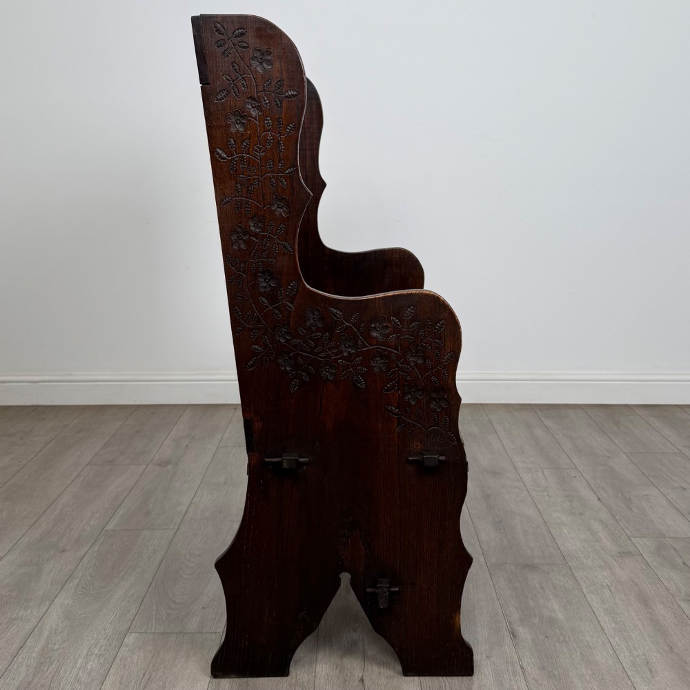 A dark oak high-back settle featuring a floral relief carving along the top rail, shaped side panels, and a stretcher base. View VII