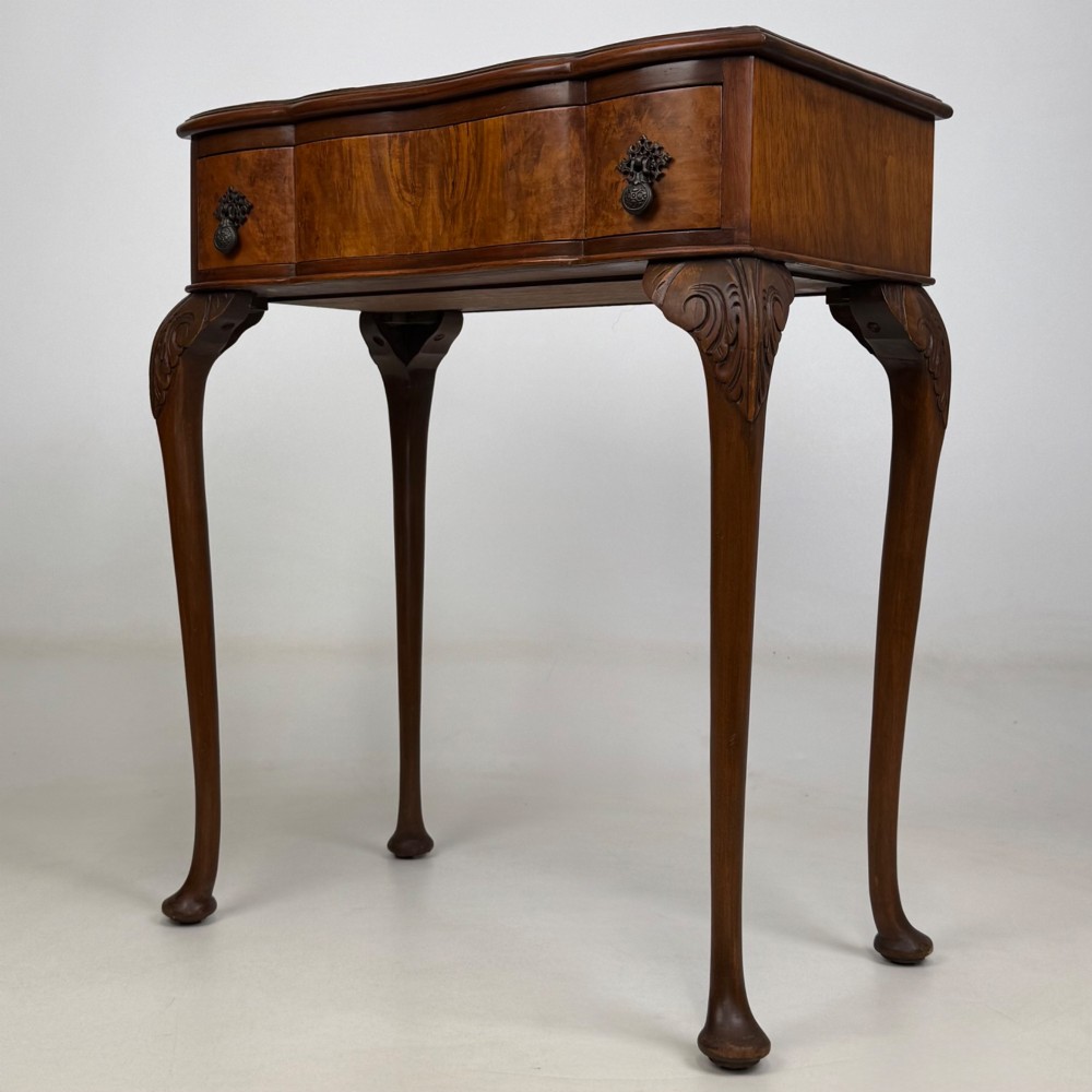An Edwardian side table crafted from warm brown figured walnut featuring a single drawer with ornate brass handles and carved cabriole legs. View II