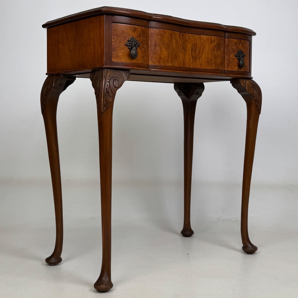 An Edwardian side table crafted from warm brown figured walnut featuring a single drawer with ornate brass handles and carved cabriole legs. View VIII