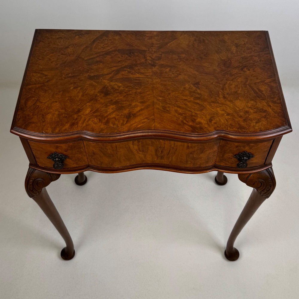 An Edwardian side table crafted from warm brown figured walnut featuring a single drawer with ornate brass handles and carved cabriole legs. View XI