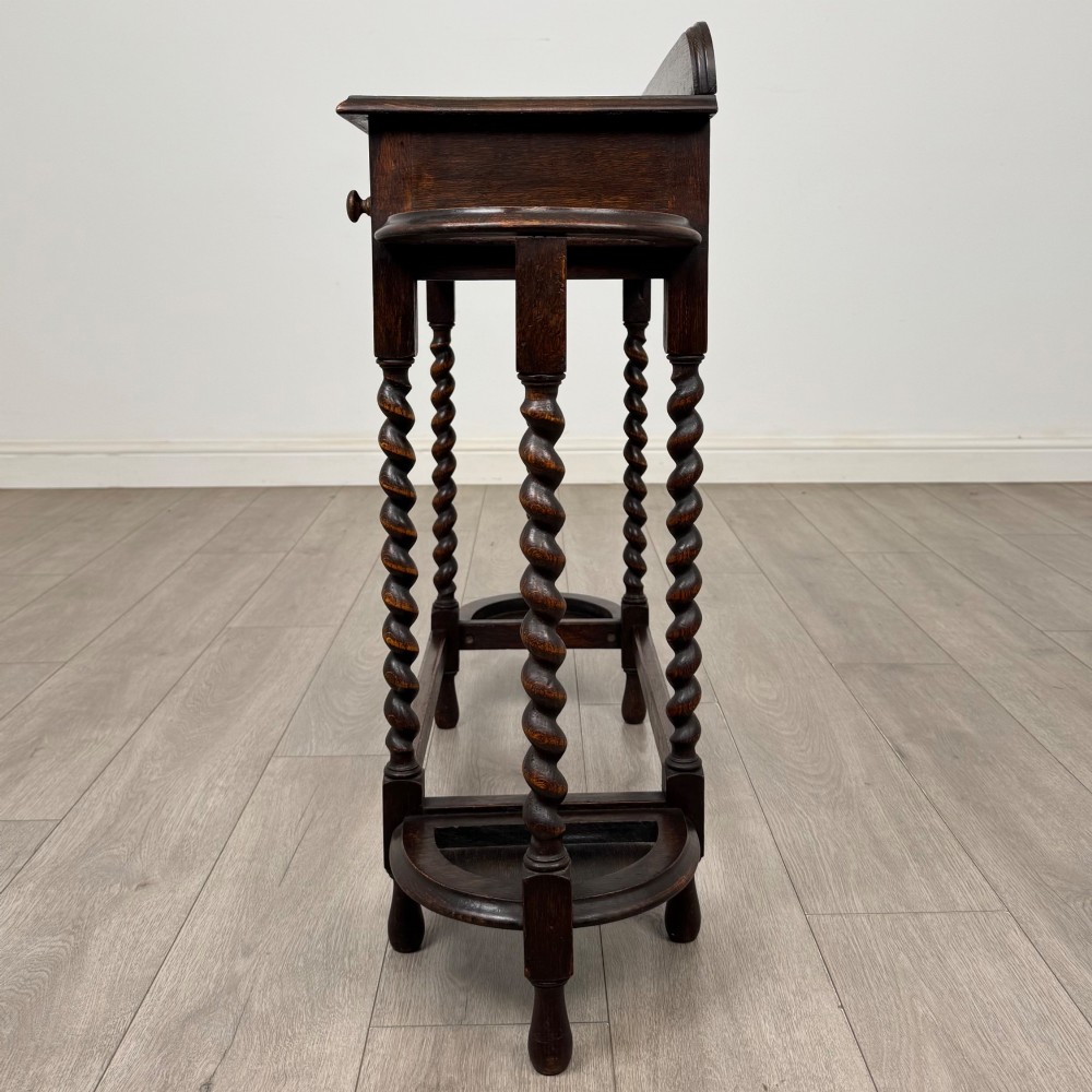 A dark oak Edwardian hall stand featuring turned barley twist legs, a central drawer with wooden knobs, and built-in side umbrella holders with drip trays. View III
