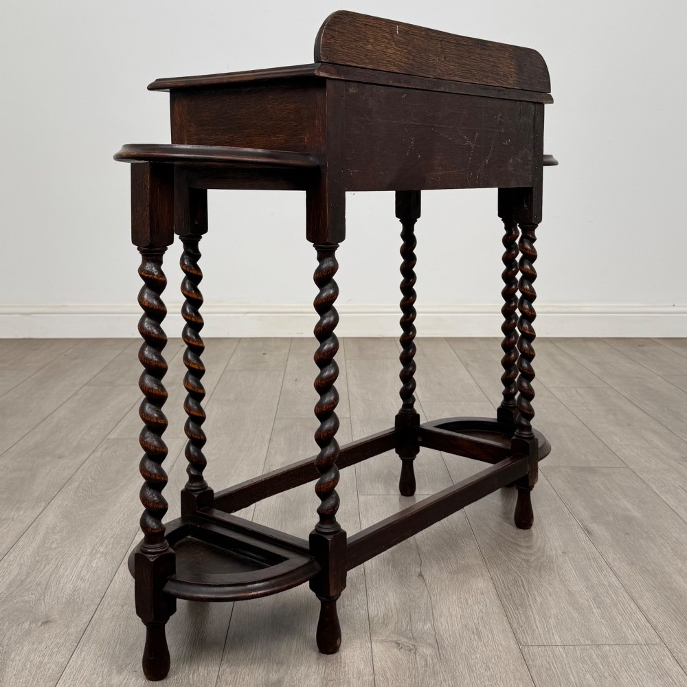A dark oak Edwardian hall stand featuring turned barley twist legs, a central drawer with wooden knobs, and built-in side umbrella holders with drip trays. View IV