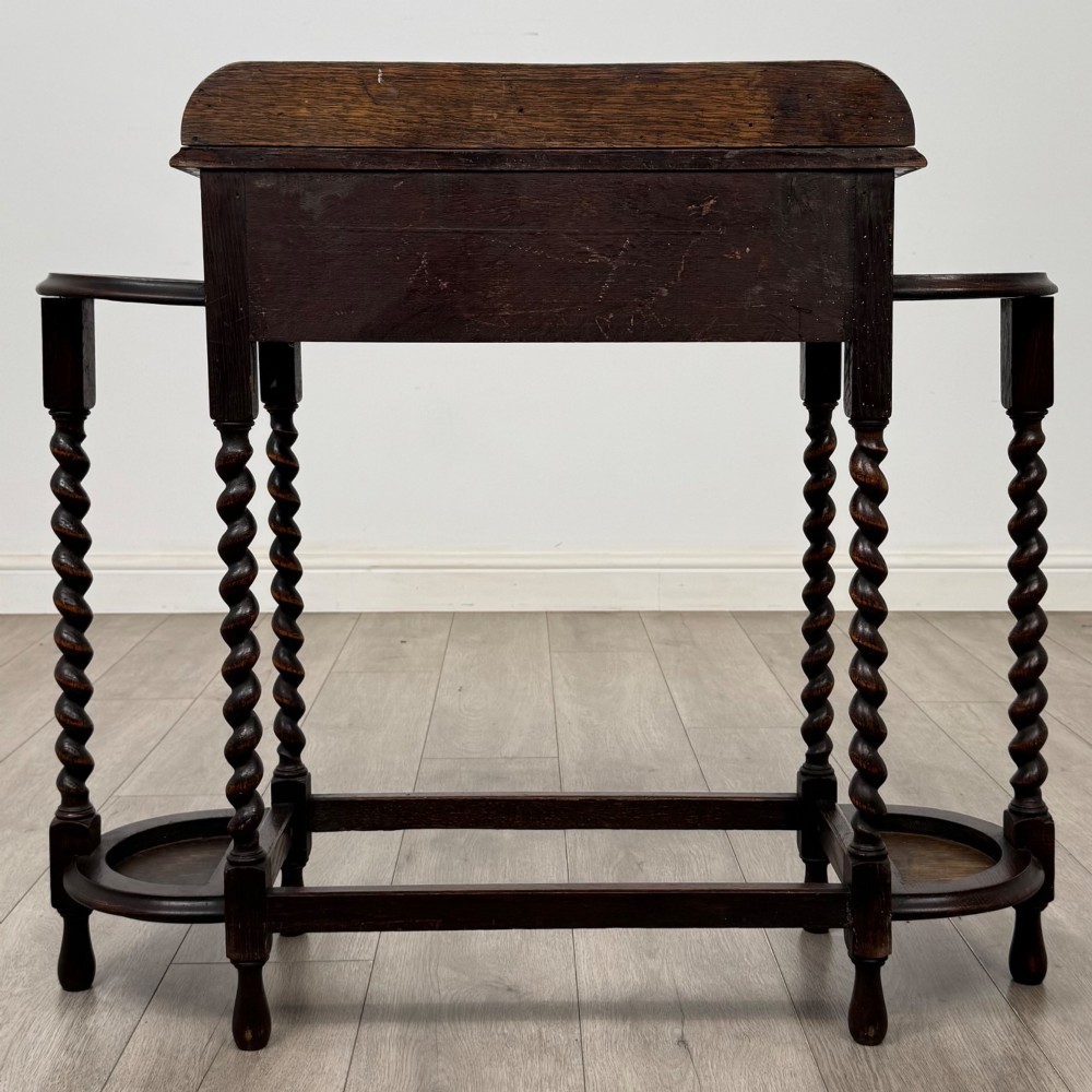 A dark oak Edwardian hall stand featuring turned barley twist legs, a central drawer with wooden knobs, and built-in side umbrella holders with drip trays. View V