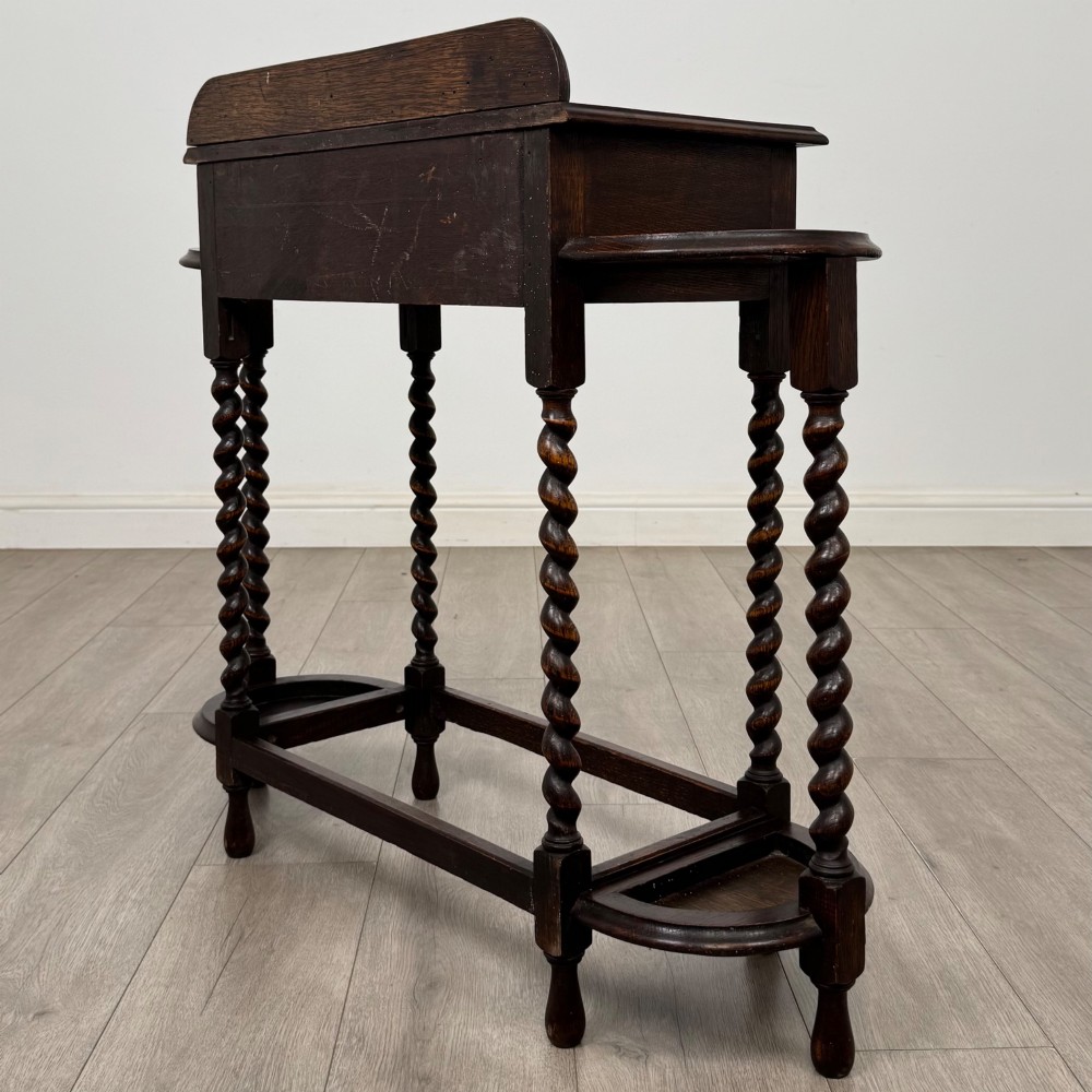 A dark oak Edwardian hall stand featuring turned barley twist legs, a central drawer with wooden knobs, and built-in side umbrella holders with drip trays. View VI