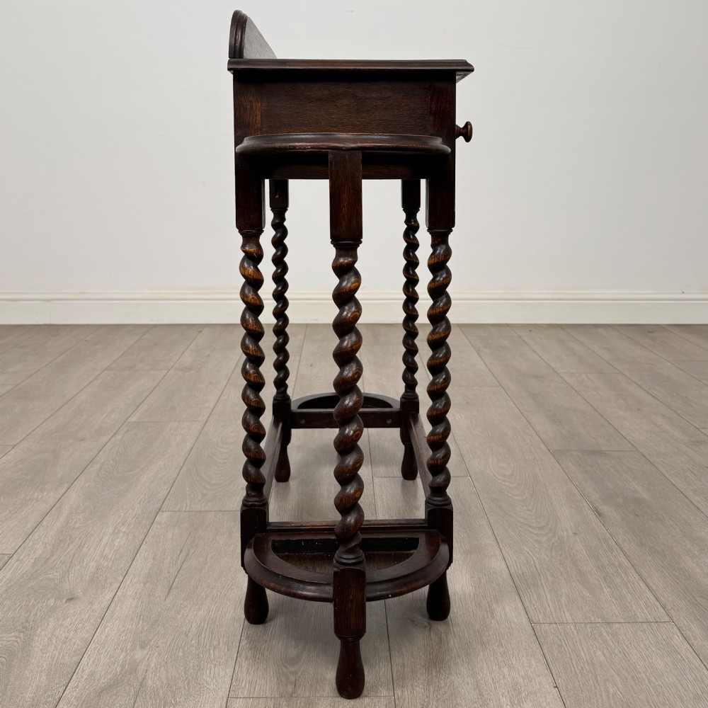 A dark oak Edwardian hall stand featuring turned barley twist legs, a central drawer with wooden knobs, and built-in side umbrella holders with drip trays. View VII