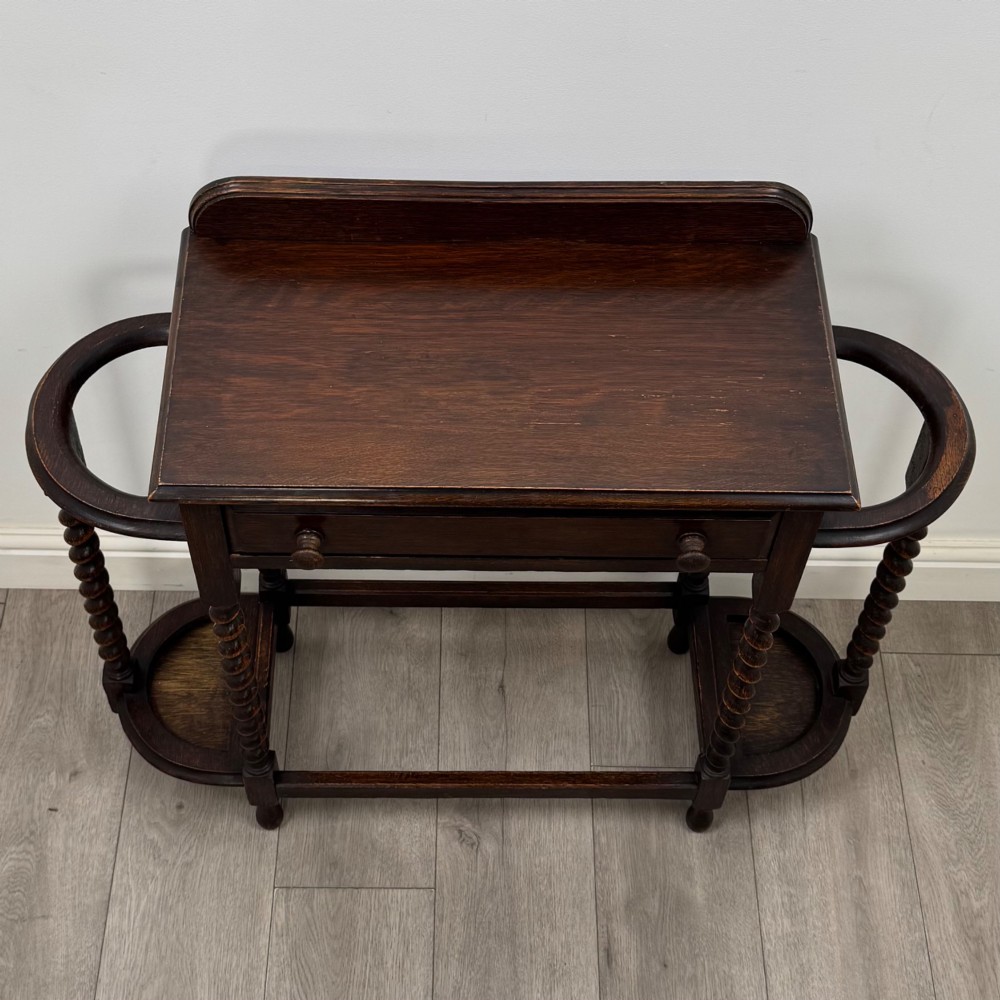 A dark oak Edwardian hall stand featuring turned barley twist legs, a central drawer with wooden knobs, and built-in side umbrella holders with drip trays. View IX