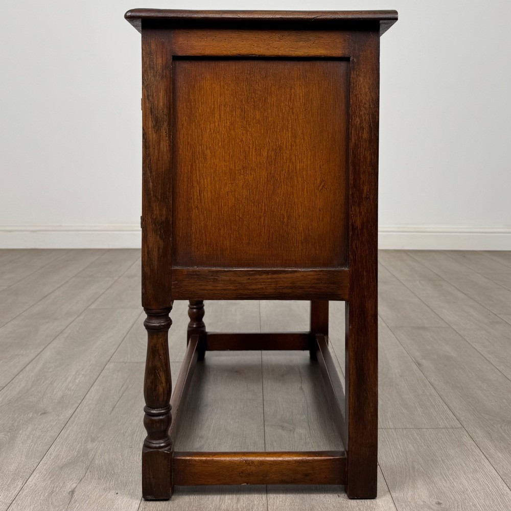 A small warm brown carved oak cupboard with double doors featuring carved arches, iron hinges, turned legs, and a lower stretcher base. View IV