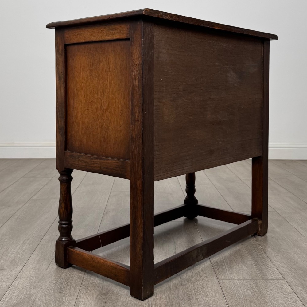 A small warm brown carved oak cupboard with double doors featuring carved arches, iron hinges, turned legs, and a lower stretcher base. View V