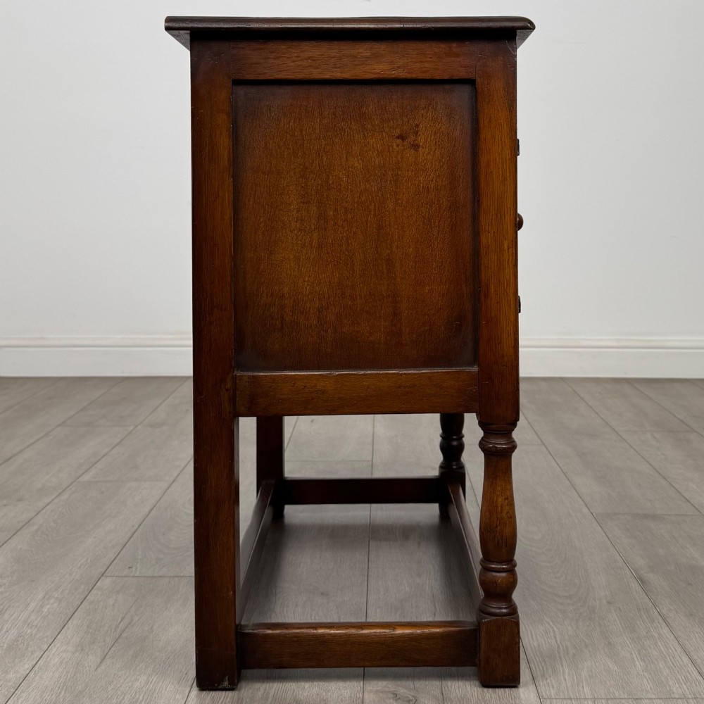 A small warm brown carved oak cupboard with double doors featuring carved arches, iron hinges, turned legs, and a lower stretcher base. View VIII