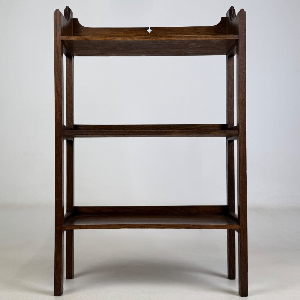 An early 20th-century Arts and Crafts solid oak open bookcase featuring three fixed shelves and a shaped gallery backboard with a cutout heart motif. View II