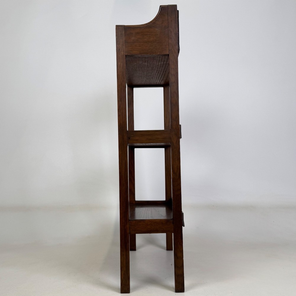 An early 20th-century Arts and Crafts solid oak open bookcase featuring three fixed shelves and a shaped gallery backboard with a cutout heart motif. View IV