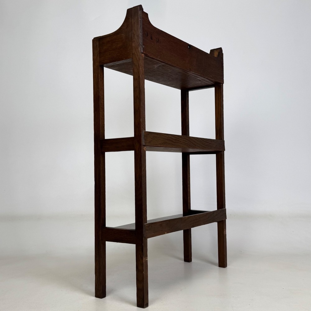An early 20th-century Arts and Crafts solid oak open bookcase featuring three fixed shelves and a shaped gallery backboard with a cutout heart motif. View V