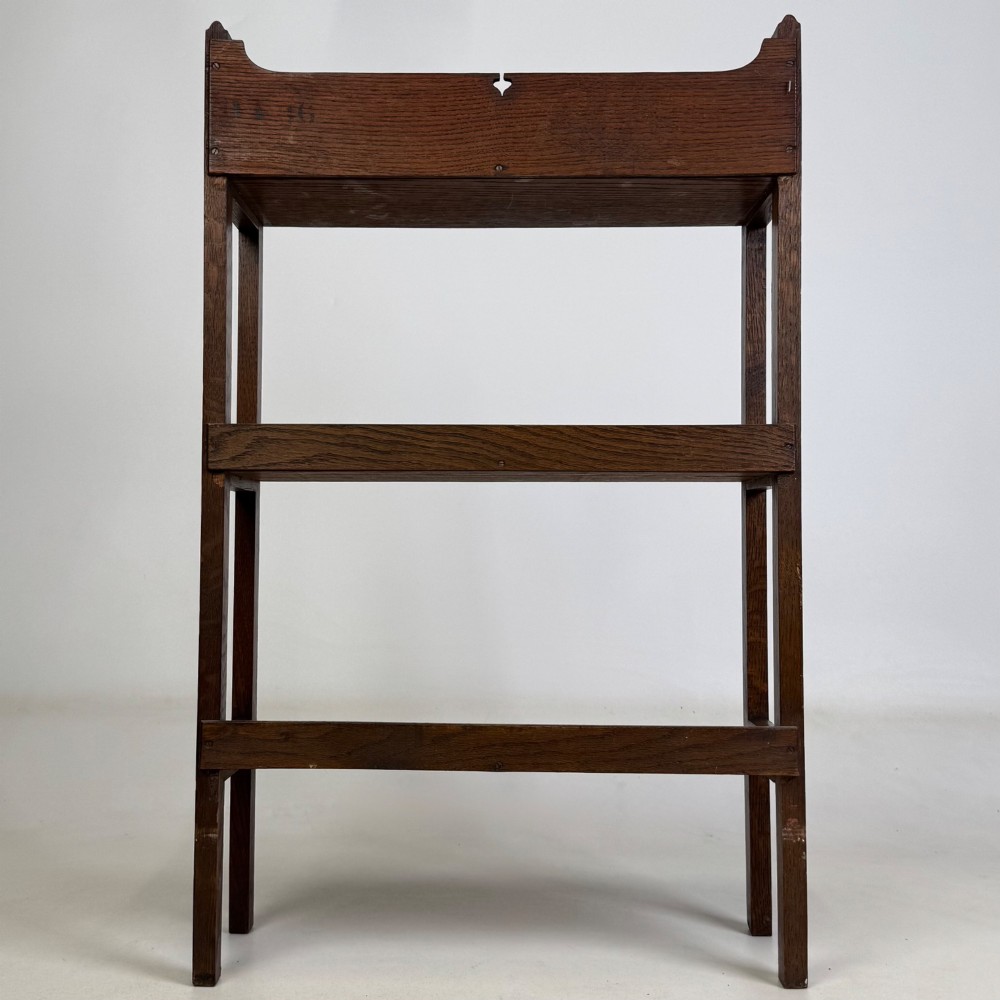 An early 20th-century Arts and Crafts solid oak open bookcase featuring three fixed shelves and a shaped gallery backboard with a cutout heart motif. View VI