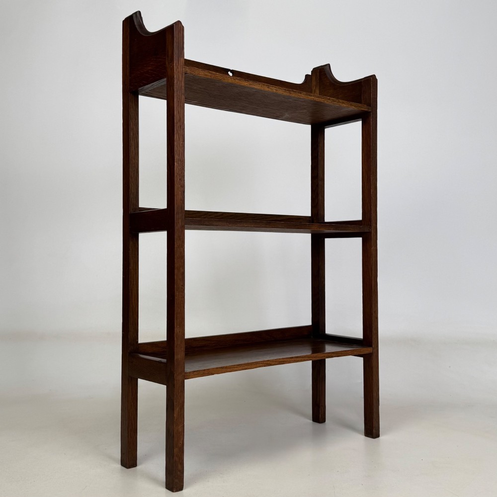 An early 20th-century Arts and Crafts solid oak open bookcase featuring three fixed shelves and a shaped gallery backboard with a cutout heart motif. View IX