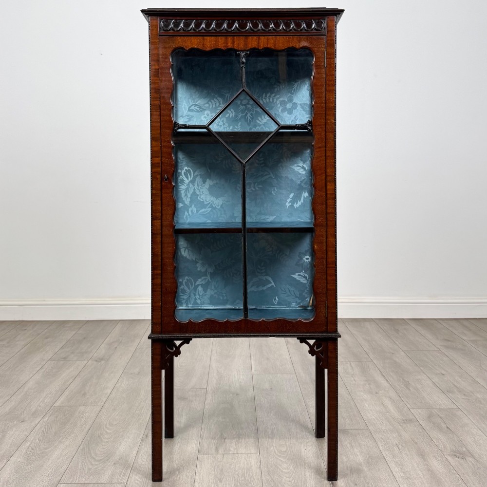 A slender Edwardian mahogany glazed display cabinet featuring astragal door bars and a fabric-lined interior raised on square legs.