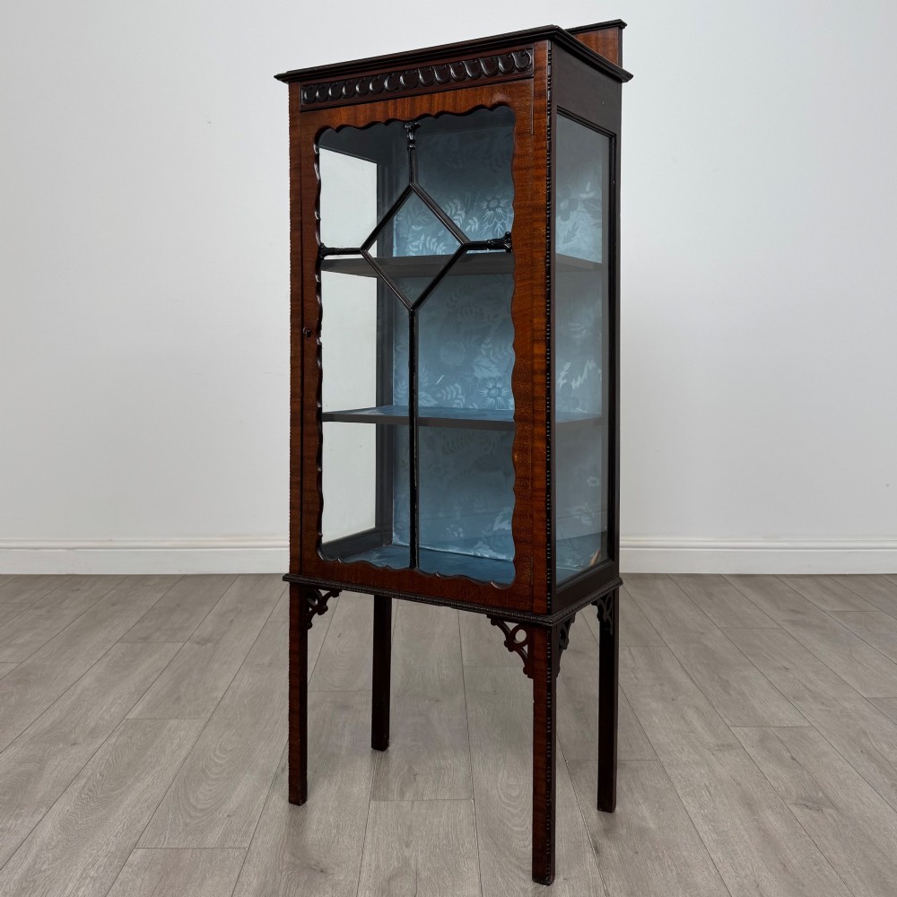 A slender Edwardian mahogany glazed display cabinet featuring astragal door bars and a fabric-lined interior raised on square legs. View III